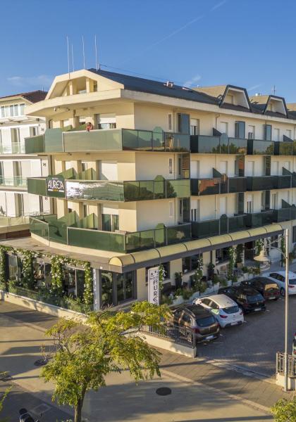 Modernes Hotel mit Balkonen und Parkplatz, von Bäumen umgeben.