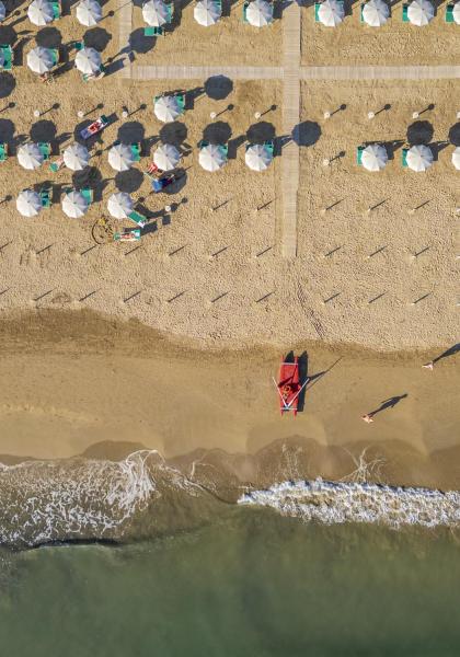 Strand mit Sonnenschirmen und ruhigem Meer, Luftaufnahme.