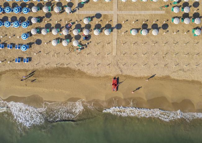 Strand mit Sonnenschirmen und ruhigem Meer, Luftaufnahme.