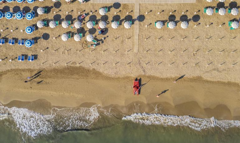 Strand mit Sonnenschirmen und ruhigem Meer, Luftaufnahme.