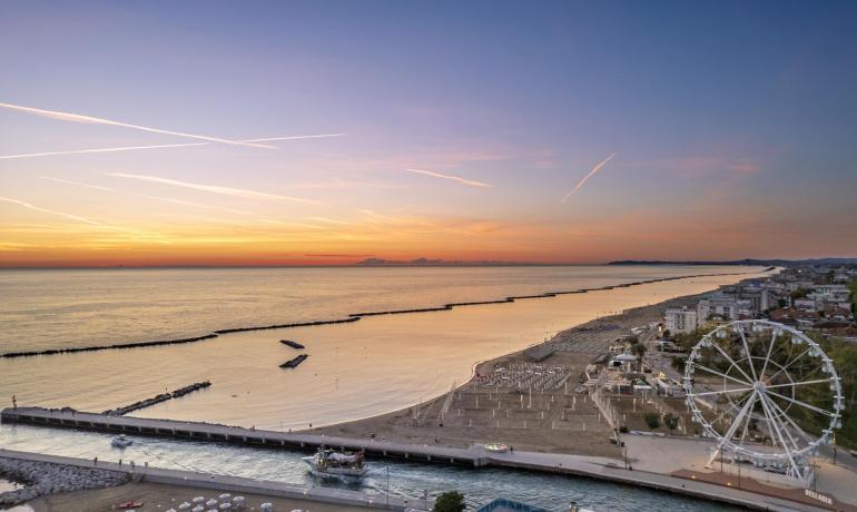 Sonnenuntergang über dem Meer mit Riesenrad und Strand.