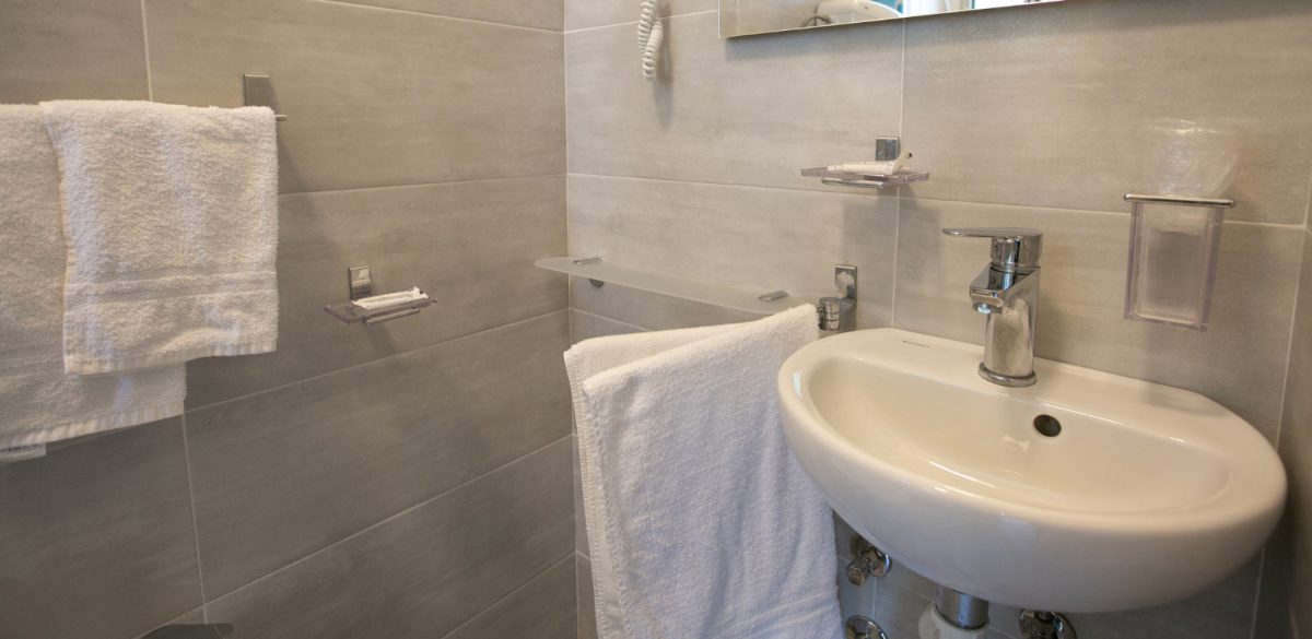 Bagno moderno con lavabo, asciugacapelli e asciugamani bianchi su pareti grigie.