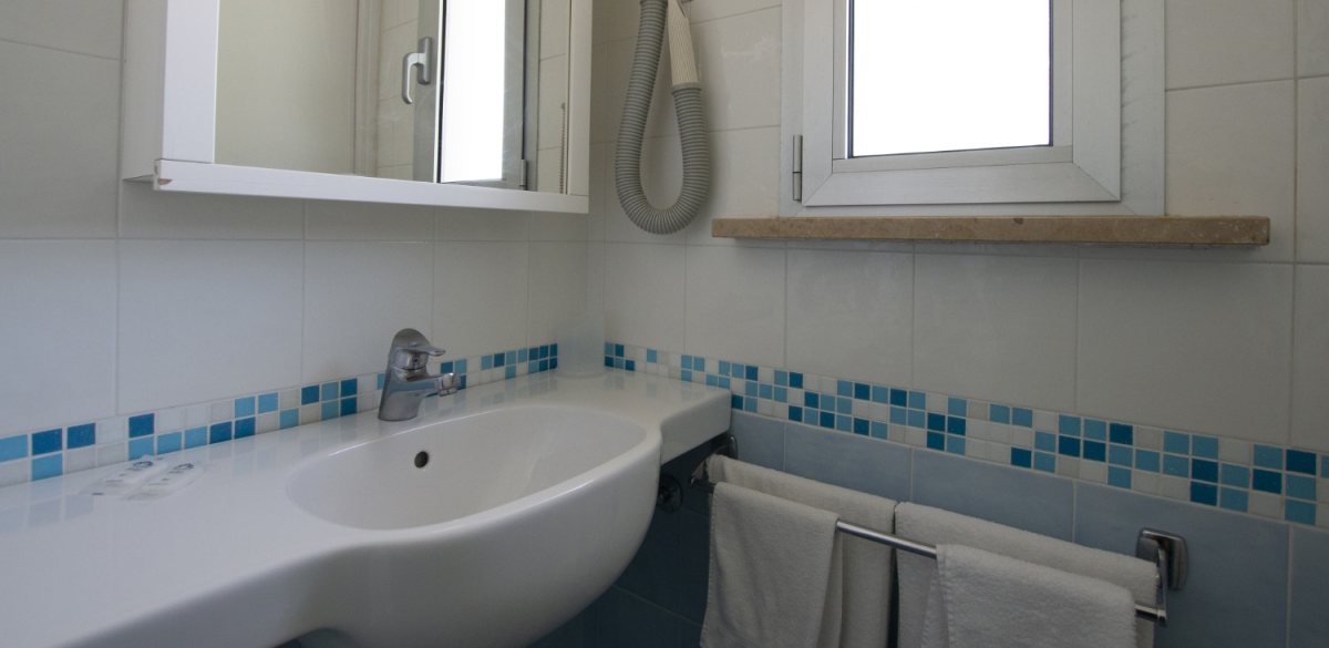 Bagno moderno con lavabo bianco, specchio, finestra e asciugacapelli a muro.