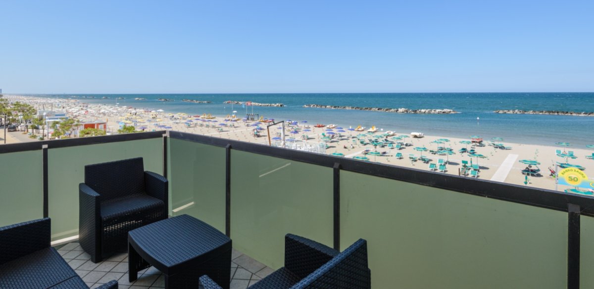 Balcone con vista mare, spiaggia attrezzata e sedie in vimini.