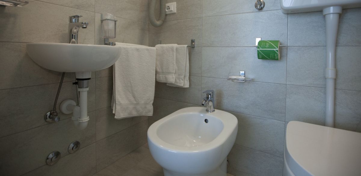 Bagno con lavabo, bidet, asciugacapelli e asciugamani appesi.