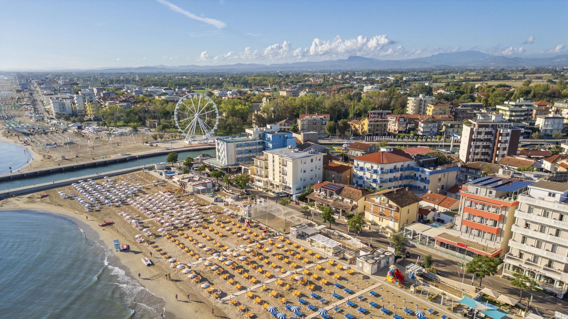 Belebter Strand mit bunten Sonnenschirmen und Riesenrad im Hintergrund.