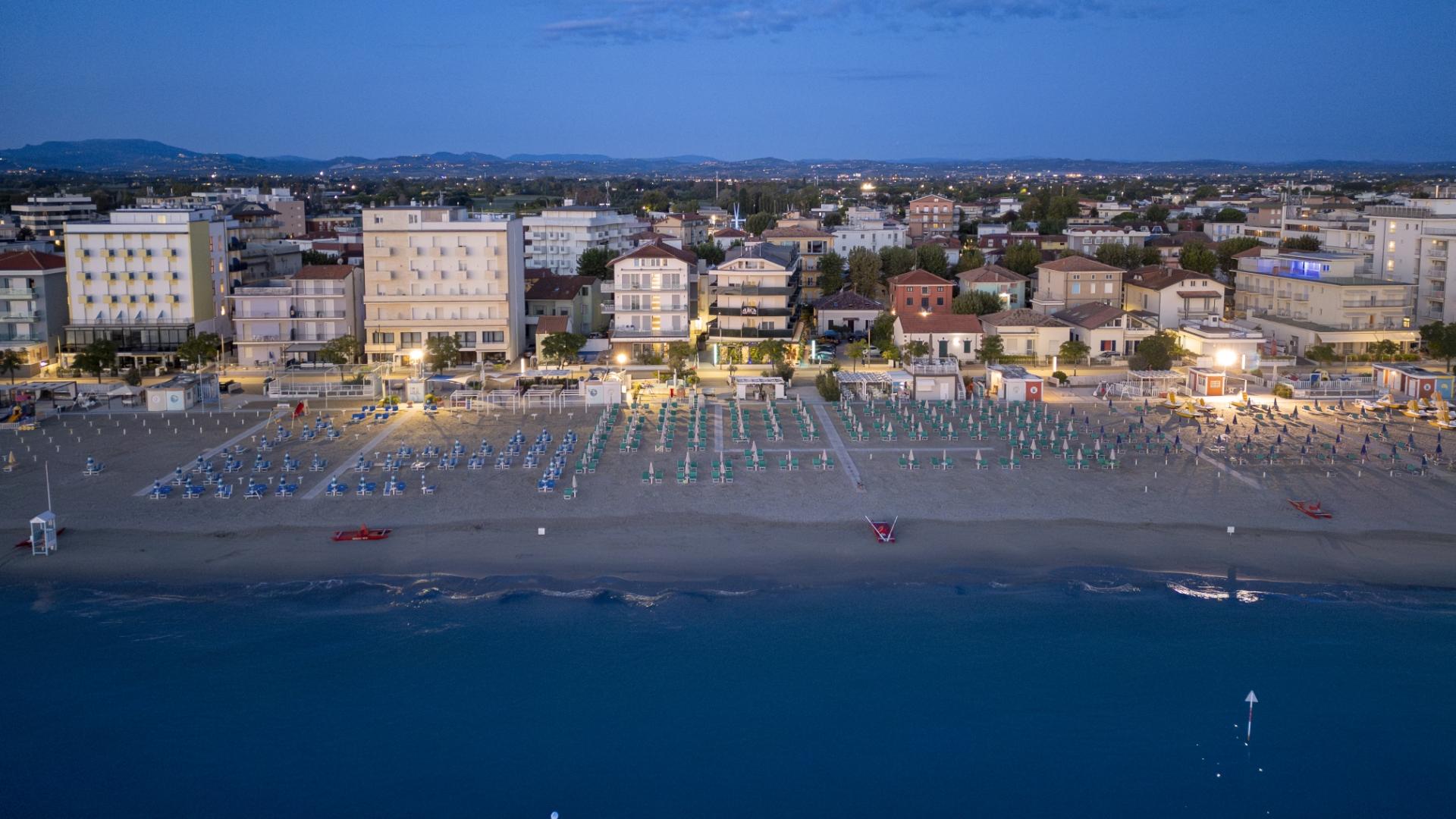 Spiaggia affollata con edifici colorati e mare calmo, vista da un frangiflutti.