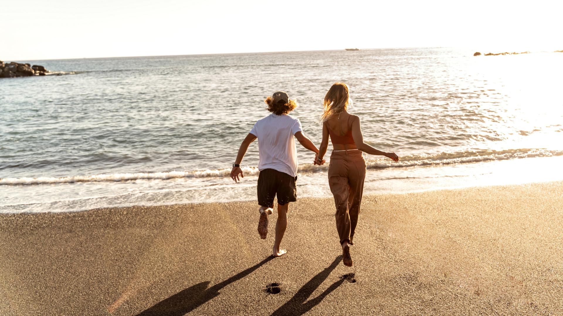 Coppia corre sulla spiaggia verso il mare al tramonto.