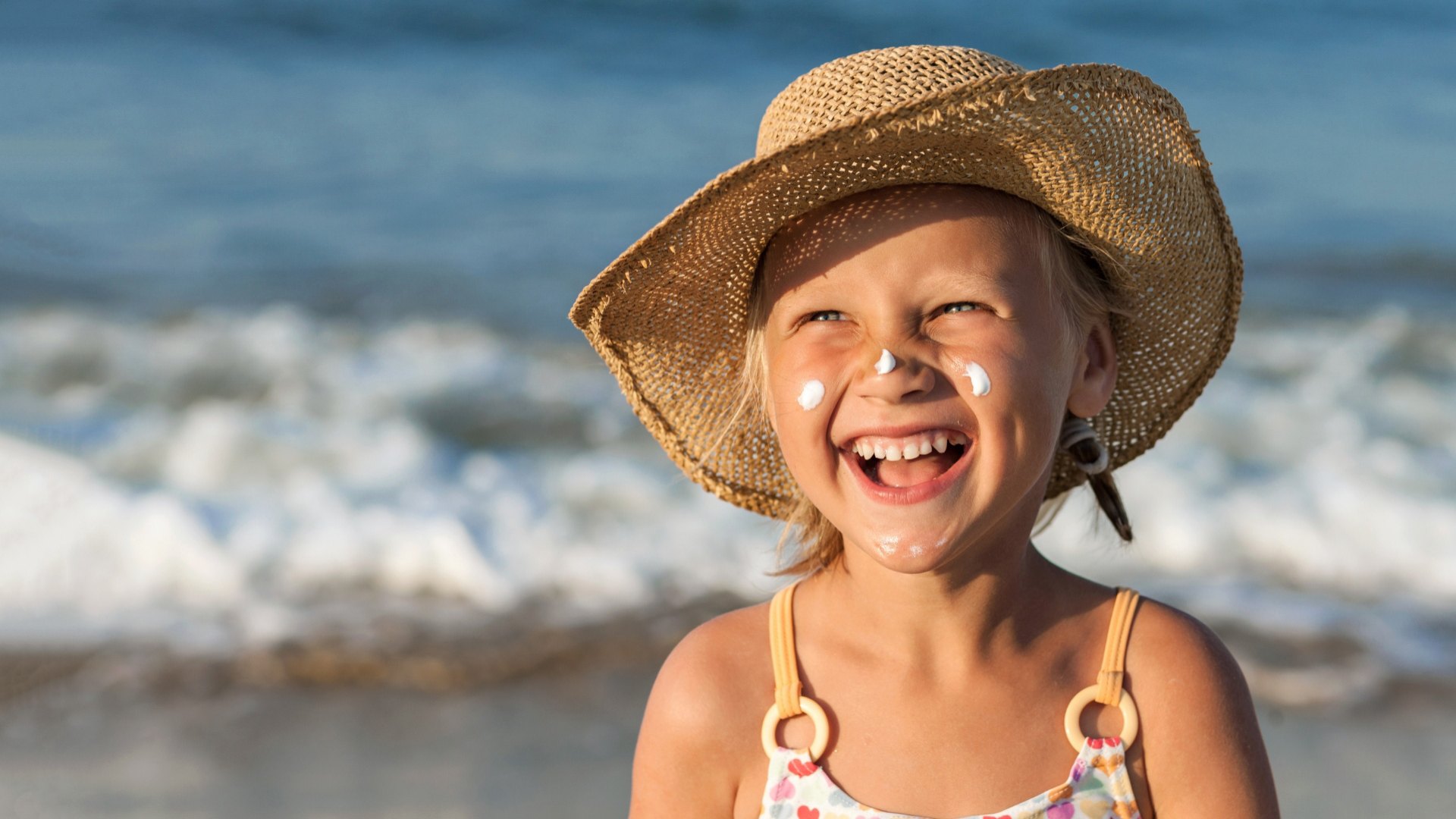 Bambina sorridente con cappello e crema solare sulla spiaggia.