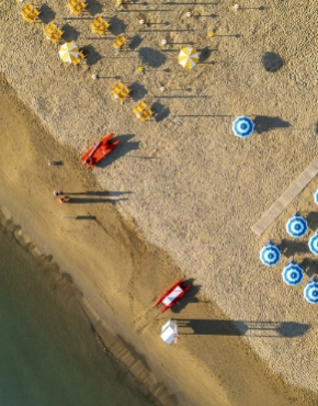 Spiaggia affollata con ombrelloni verdi e bianchi, mare calmo e scogliere sullo sfondo.