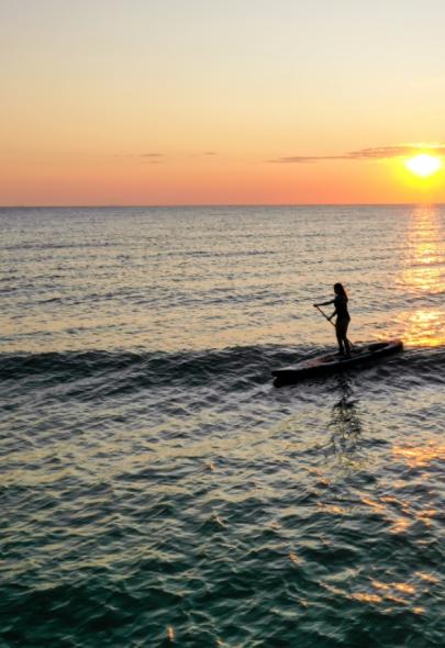 Persona fa paddleboard al tramonto sull'oceano.