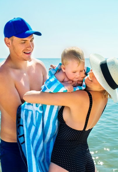 Famiglia in spiaggia, genitori con bambino avvolto in un asciugamano blu.