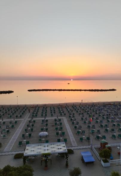 Spiaggia al tramonto con file di lettini e mare calmo all'orizzonte.