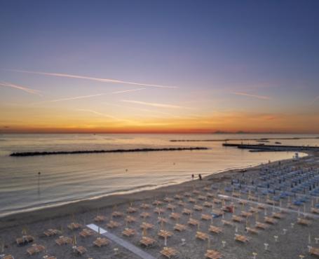 Spiaggia all'alba con ombrelloni e mare calmo, vista su barriere frangiflutti.