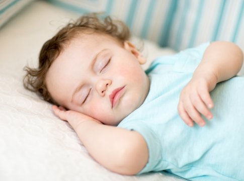 Bambino che dorme serenamente su un letto, indossando una maglietta azzurra.