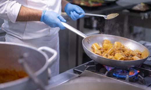 Chef cucina pasta in padella con guanti blu.