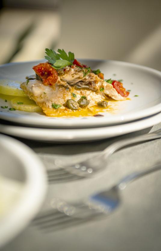 Piatto di pesce con capperi, pomodori e prezzemolo.