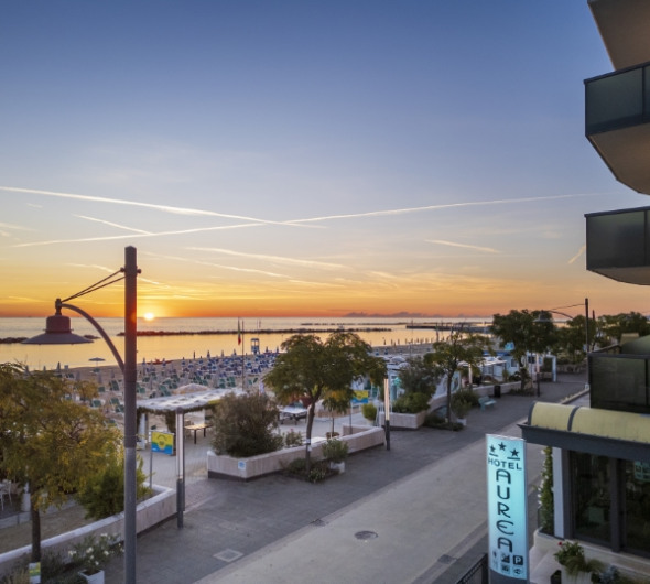 Alba sul mare con barca e scogliere, cielo dai colori caldi.