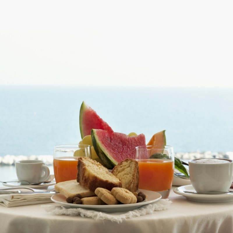 Colazione con frutta, succo, caffè e biscotti vista mare.