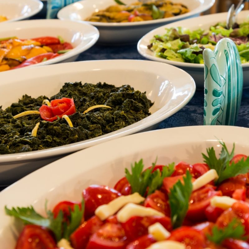 Piatti di verdure assortite su un tavolo, con insalate e spinaci.